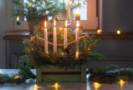 Photo for Advent decoration with fir branches and four burning candles in wooden basket on white table at home - Royalty Free Image