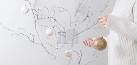 Foto de Mujer joven con bola de Navidad y rama blanca interior - Imagen libre de derechos