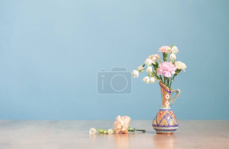 Photo for Flowers in vintage jug on wooden table on blue background - Royalty Free Image