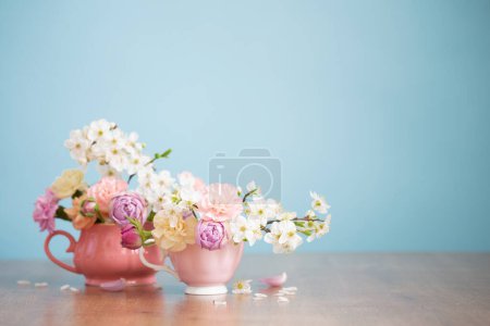 Foto de Hermosas flores de primavera en dos tazas en colores pastel sobre fondo azul - Imagen libre de derechos
