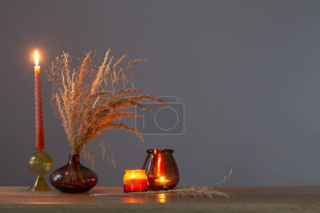 Foto de Flores secas y velas encendidas en la pared oscura de fondo - Imagen libre de derechos