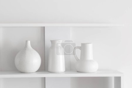 Téléchargez les photos : Vases en céramique blanche sur étagère en bois sur mur blanc - en image libre de droit