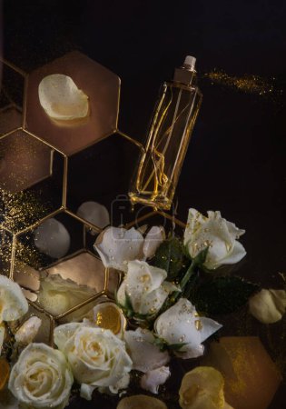 Téléchargez les photos : Bouteille de parfum au parfum de miel et de roses sur fond sombre - en image libre de droit