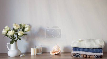 Photo for Knitted clothing and white roses in jug on modern dresser - Royalty Free Image