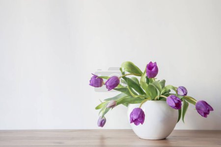 tulipanes morados en jarrón de cerámica blanca en estante de madera