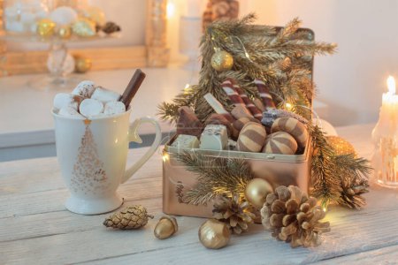 Foto de Dulces de Navidad en caja dorada y taza de cacao con malvaviscos en una mesa blanca - Imagen libre de derechos