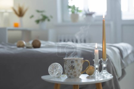 Photo for Cup of coffee with christmas balls on little table in white bedroom - Royalty Free Image