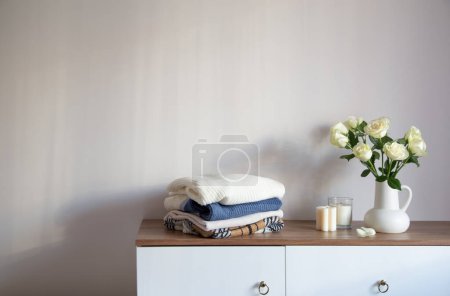 Foto de Ropa de punto y rosas blancas en jarra en cómoda moderna - Imagen libre de derechos