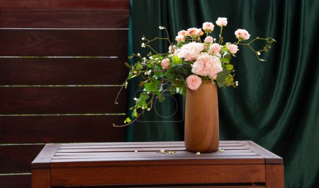 Foto de Rosas rosadas con hiedra en jarrón en estante de madera en la pared derk fondo y cortina verde - Imagen libre de derechos