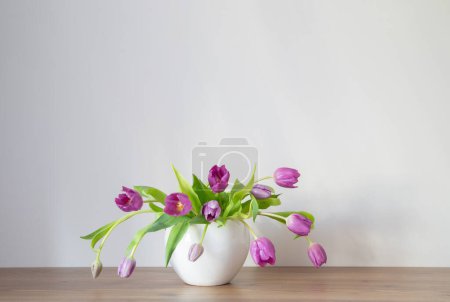 Foto de Tulipanes morados en jarrón de cerámica blanca en estante de madera - Imagen libre de derechos
