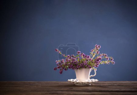 Photo for Thyme flowers in white vintage cup on wooden table on blue background - Royalty Free Image