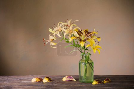 Téléchargez les photos : Lys jaune dans un vase en verre vert sur une table en bois - en image libre de droit