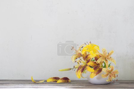 Foto de Lirio amarillo en jarrón blanco de cerámica sobre mesa de madera - Imagen libre de derechos
