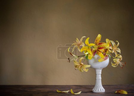 Téléchargez les photos : Lys jaune dans un vase blanc en céramique sur une table en bois - en image libre de droit