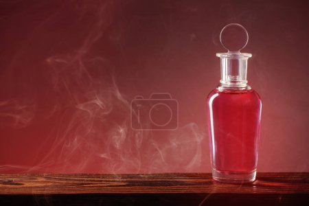 Foto de Botella con poción mágica en humo sobre fondo rojo - Imagen libre de derechos