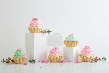 Téléchargez les photos : Cupcakes roses et verts avec des fleurs printanières sur des podiums en bois sur fond blanc - en image libre de droit
