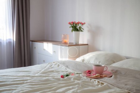 Foto de Taza de café rosa en la cama con flores en jarrón en el dormitorio blanco - Imagen libre de derechos