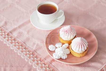 Foto de Cupcakes blancos y rosados y taza de té en mantel vintage - Imagen libre de derechos