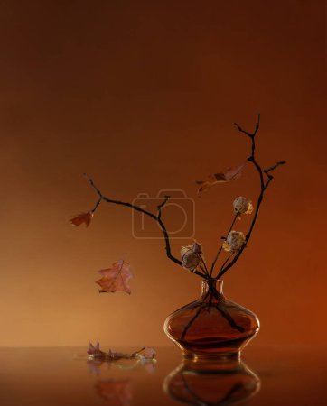 Foto de Bodegón de otoño con rosas secas y hojas de roble en jarrón de vidrio - Imagen libre de derechos