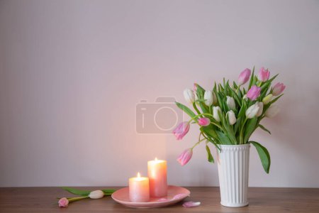 Foto de Tulipanes de primavera en jarrón con velas encendidas en estante de madera - Imagen libre de derechos