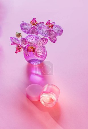 Téléchargez les photos : Baume à lèvres avec orchidée dans un vase en verre sur fond rose - en image libre de droit