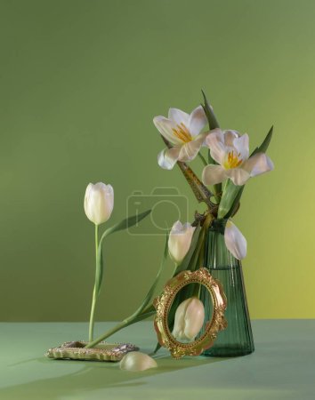 Photo for Freakebana with white tulips in green glass vase on green background - Royalty Free Image