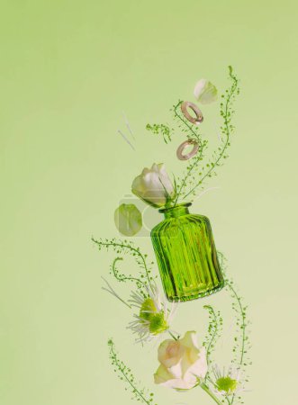 Téléchargez les photos : Fleurs volantes dans un vase en verre vert sur fond vert - en image libre de droit