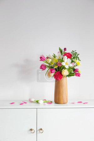 Foto de Hermosas flores en jarrón en el estante en la pared blanca de fondo - Imagen libre de derechos