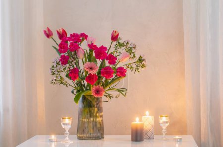 Photo for Pink flowers in glass modern vase with burning candles in white interior - Royalty Free Image