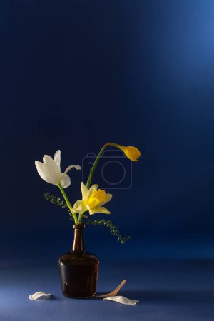 Photo for Spring flowers in glass bottle on dark blue background - Royalty Free Image