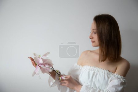 Foto de Mujer joven elegante en vestido blanco con flores de primavera en jarrones sobre fondo gris - Imagen libre de derechos