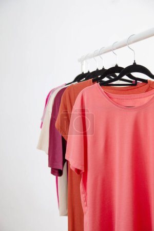 Photo for Row of t-shirts on a hanger against a background of a white wall hanger - Royalty Free Image