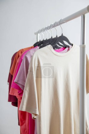 Reihe von T-Shirts auf einem Kleiderbügel vor dem Hintergrund eines weißen Wandhängers