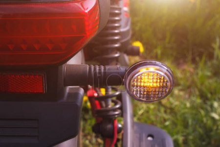 Téléchargez les photos : Le clignotant droit du scooter ou du vélo stationné sur le bord de la route. La vue rapprochée du signal de sécurité de direction avec l'environnement d'été extérieur. - en image libre de droit