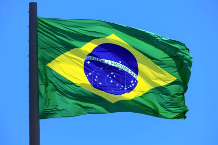 Foto de Bandera brasileña ondeando en el viento sobre el fondo azul del cielo. Bandera de Brasil. - Imagen libre de derechos