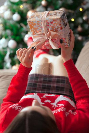 Téléchargez les photos : Fille en pull rouge avec un cadeau sur le fond de l'arbre de Noël - en image libre de droit