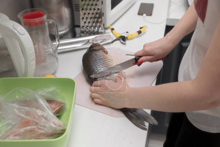 Téléchargez les photos : Femme au foyer préparant la nourriture à la cuisine, coupant du poisson frais - en image libre de droit