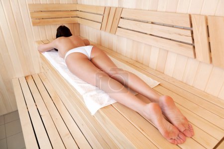 Photo for Woman relaxing in a sauna. She is lying on a towel. - Royalty Free Image