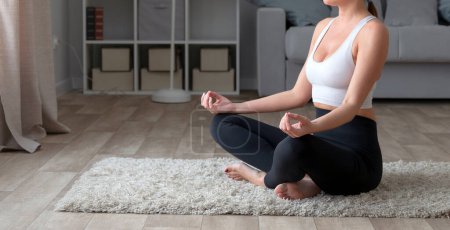 Foto de Mujer joven y deportiva practicando yoga en casa, sentada en posición de loto - Imagen libre de derechos