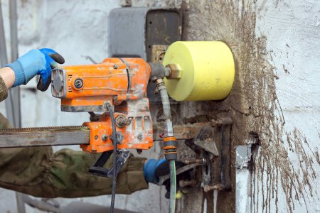 Arbeiter mit einer elektrischen Bohrmaschine, um ein Loch in eine Betonwand zu bohren, Nahaufnahme
