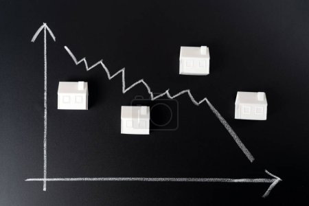 Foto de Decreasing house prices concept metaphor shown from plastic miniature houses and line graph on black board - Imagen libre de derechos