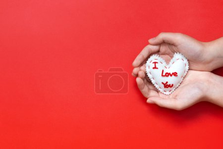 Photo for I Love You sewn valentines heart cupped in hands on red background - Royalty Free Image