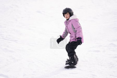 Téléchargez les photos : Action motion photo d'une enfant asiatique snowboarder sur la piste de ski de montagne faisant style snowboard gratuit. - en image libre de droit