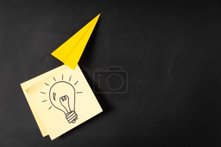 Téléchargez les photos : Origami avion en papier porte un symbole d'ampoule dessiné à la main sur papier jaune collant note, concepts de nouvelle idée, unique, créative ou innovante dans le succès de l'entreprise, la croissance du marketing - en image libre de droit