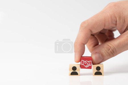 Téléchargez les photos : Main met un cube en bois avec symbole d'icône d'accord de poignée de main entre deux cubes d'icône de personne, concept d'accord d'affaires, affaire, partenariat ou coopération entre les parties. - en image libre de droit