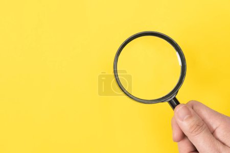 Téléchargez les photos : Main d'homme tenant une loupe de style classique isolée sur fond jaune, espace de copie pour le texte - en image libre de droit