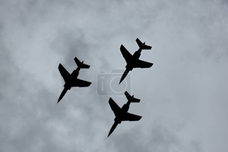 Téléchargez les photos : Avions de chasse à réaction silhouette contre ciel nuageux sombre, volant en formation étroite - en image libre de droit
