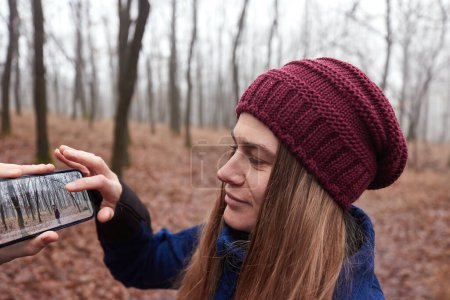Téléchargez les photos : Randonnée dans la forêt d'automne, femme regarder des photos d'elle prises avec un téléphone portable - en image libre de droit
