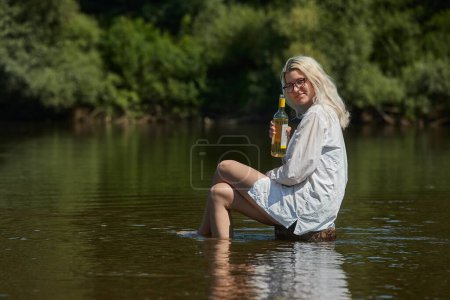 Foto de Mujer joven relajándose en el río con una botella de vino - Imagen libre de derechos