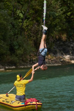 Téléchargez les photos : Solkan, Slovénie - Vers 2022 : Un homme aide une fille à monter dans un bateau sur la rivière lorsqu'elle est suspendue à un cordon élastique après avoir sauté du pont Solkan - en image libre de droit